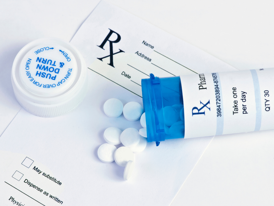 Prescription pill bottle, spilled white tablets, and blue-capped medicine tube on a white background
