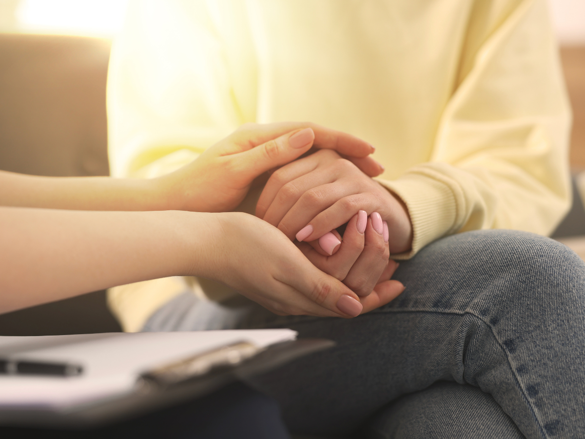 Two people holding hands in a warm, supportive counseling setting