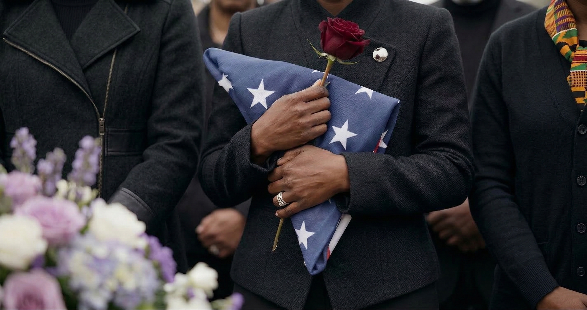 Mourners in black hold folded American flags and flowers during a memorial service