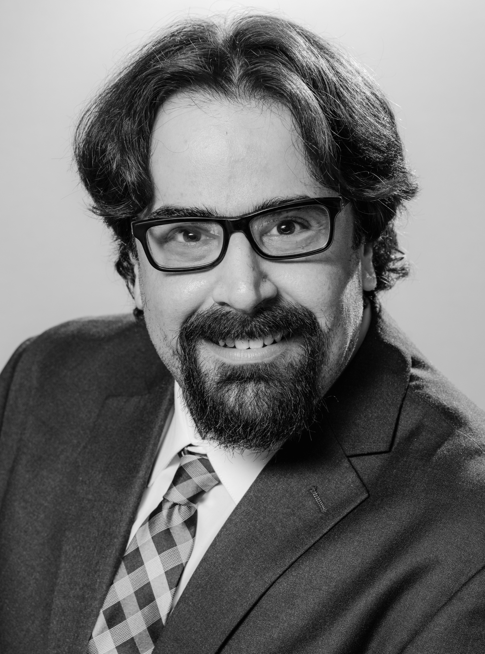 Man in glasses and suit jacket smiling against a plain background