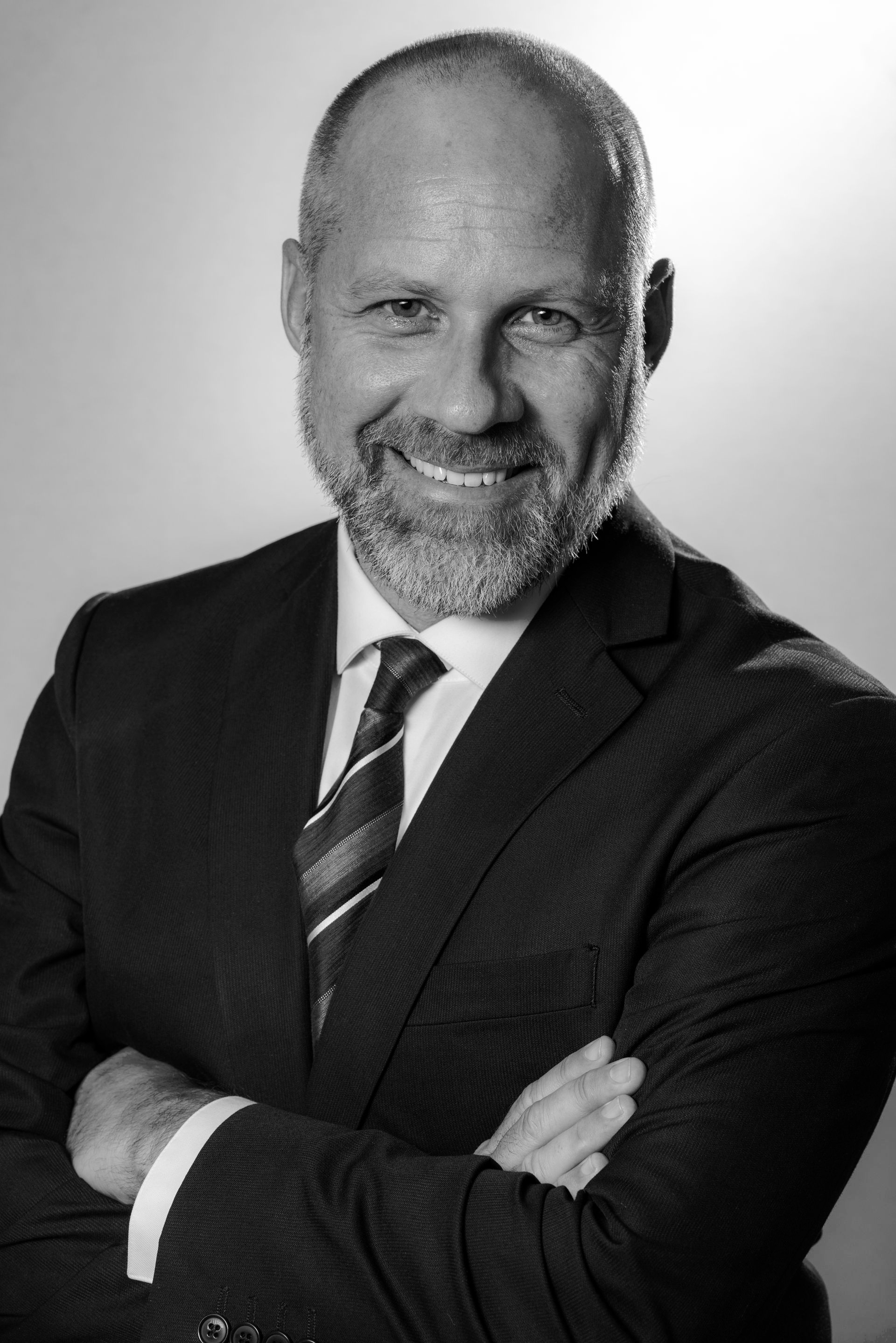 Portrait of a smiling man in a dark suit with arms crossed on a light background
