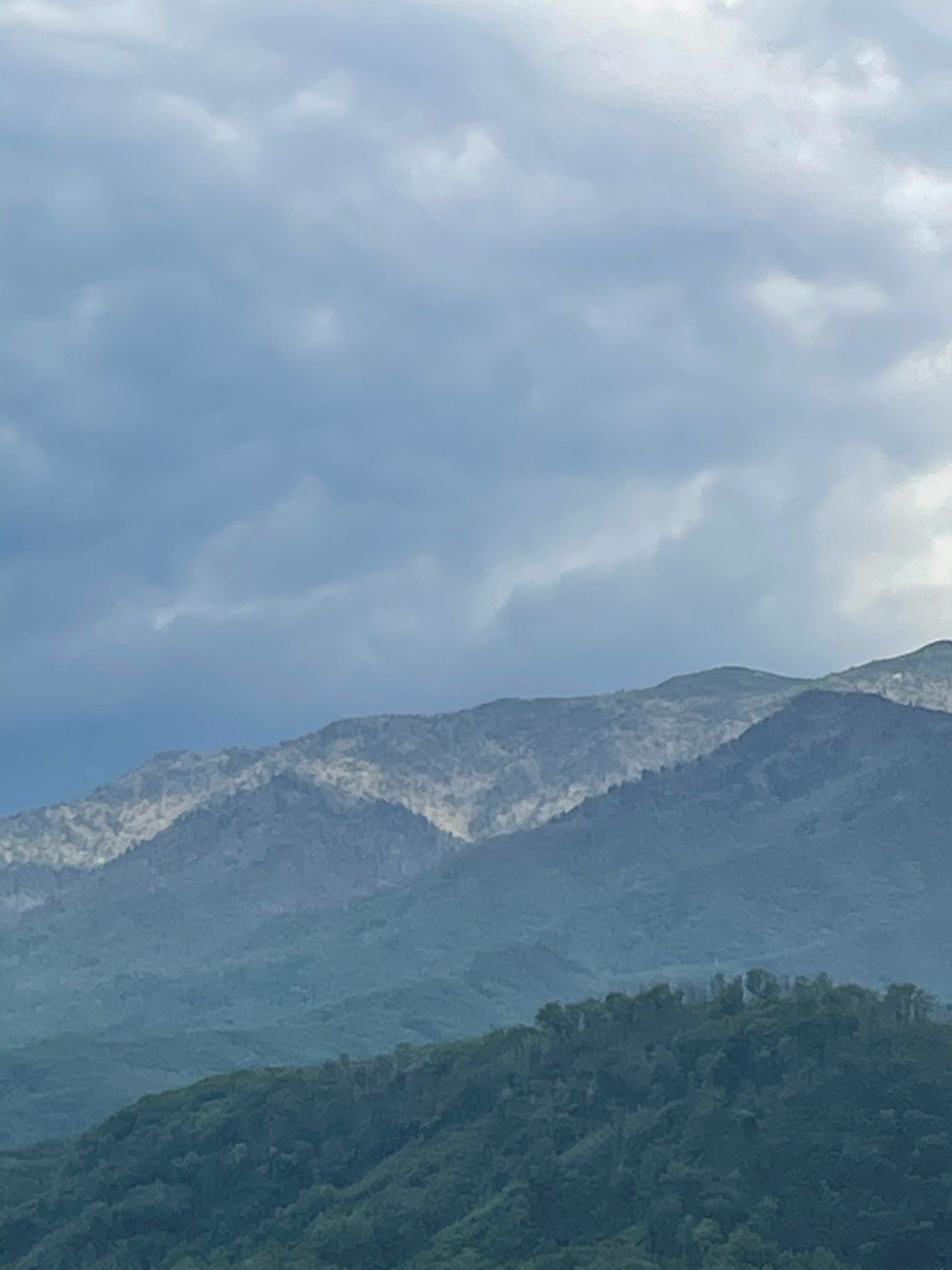 Cloudy mountain landscape with layered green hills and a rocky ridge under overcast sky