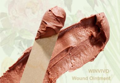 Brown wound ointment spread on a wooden applicator, with a blurred floral background.