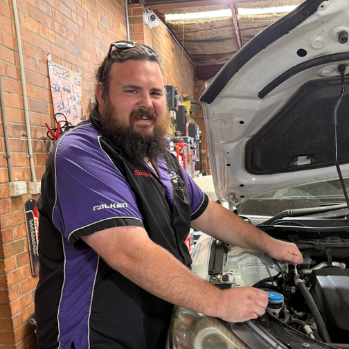 Mechanic in a purple shirt working under a car hood in a garage