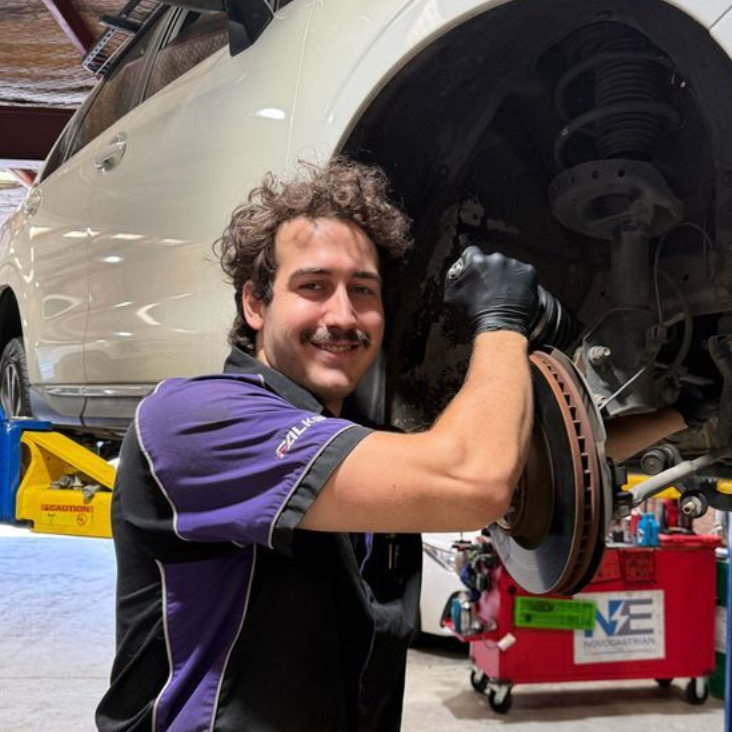Mechanic smiling beside a car’s exposed brake rotor in an auto shop