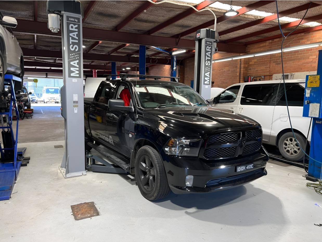 Black Pickup Truck on A Lift Inside a Garage, with A White Van and Tools Visible — AutoHop Lambton