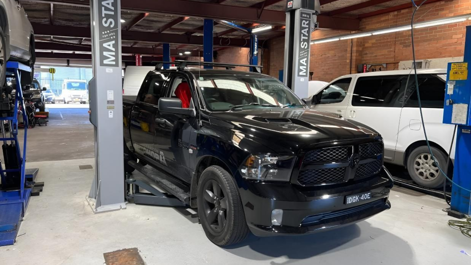 Black SUV in an auto service bay with a white van parked beside it