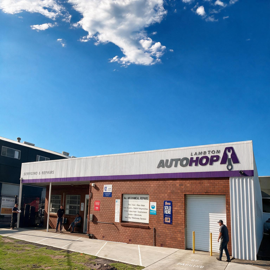 Black pickup truck with bull bar parked beside a purple-and-white warehouse on a wet lot
