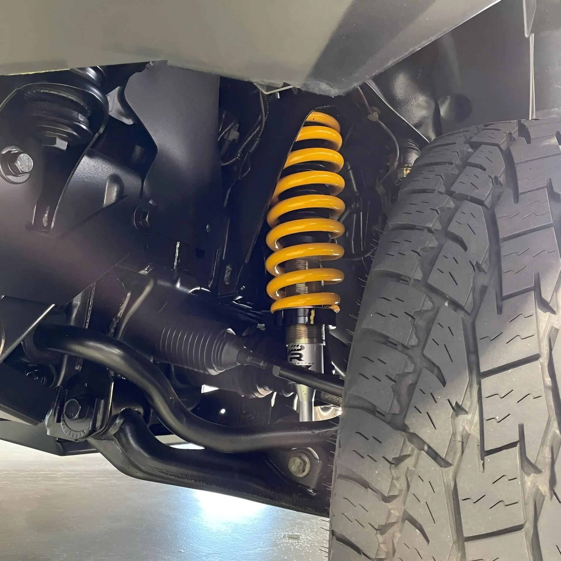 Close-up of a vehicle suspension with a yellow coil spring beside a tire undercarriage.