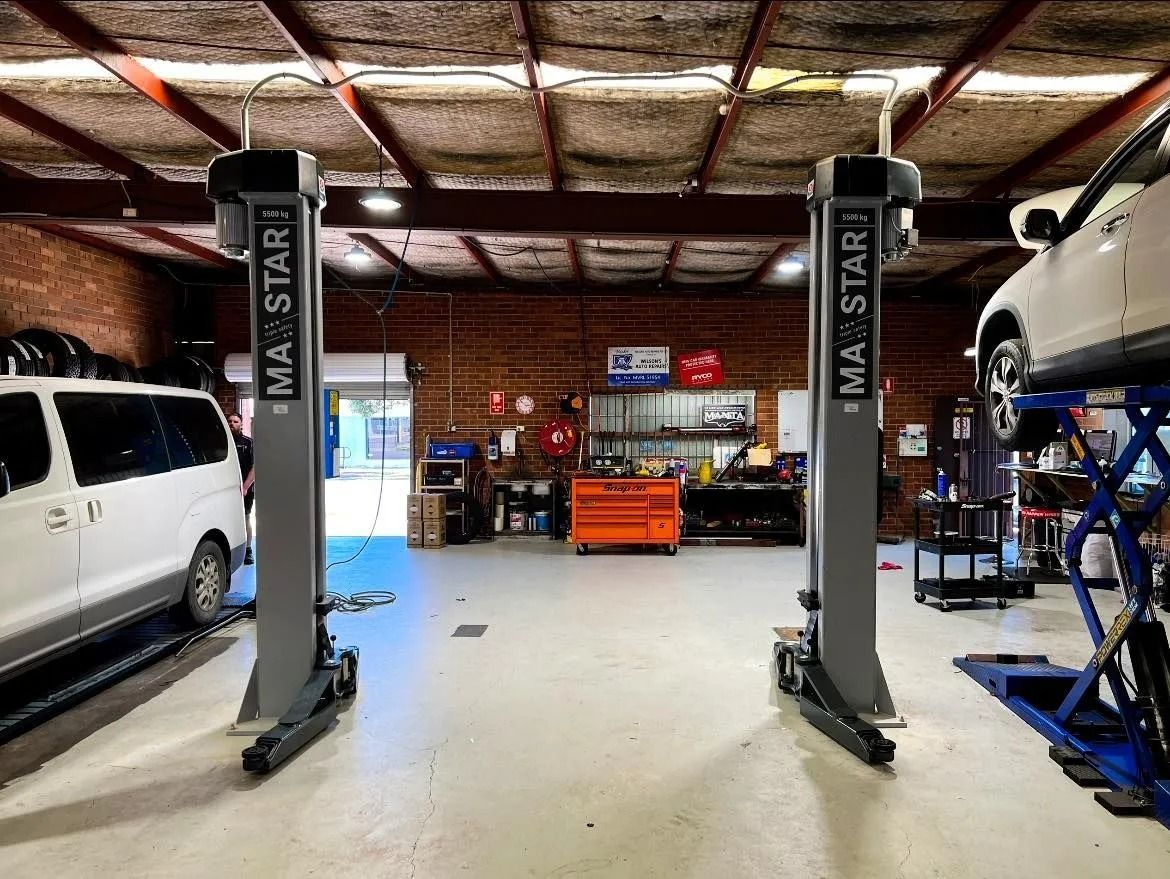 Car repair shop interior with two vehicle lifts, a white van on the left, and a lifted car on the right.