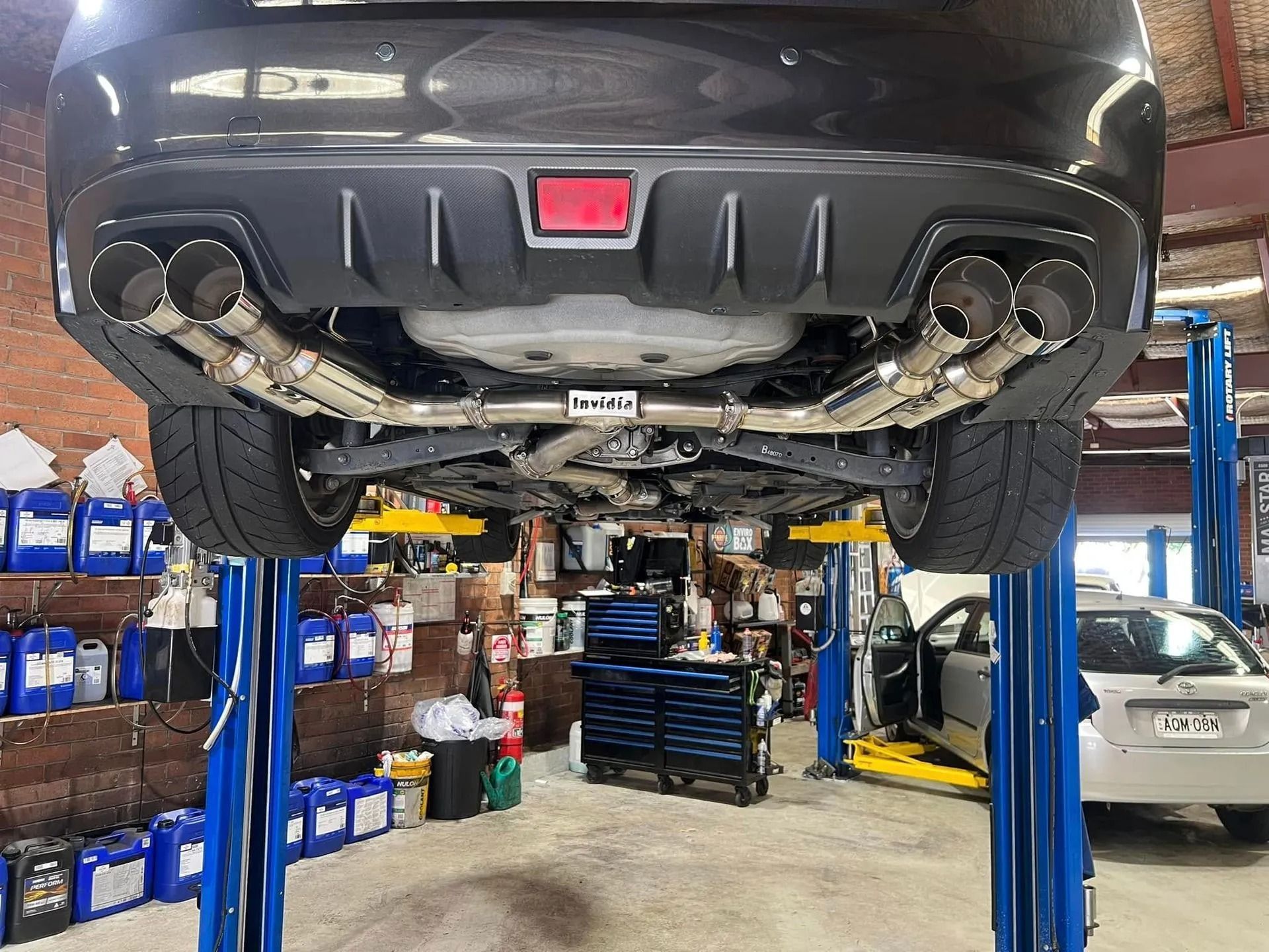 Black car lifted on a repair hoist in an auto shop, rear view with exposed exhaust system