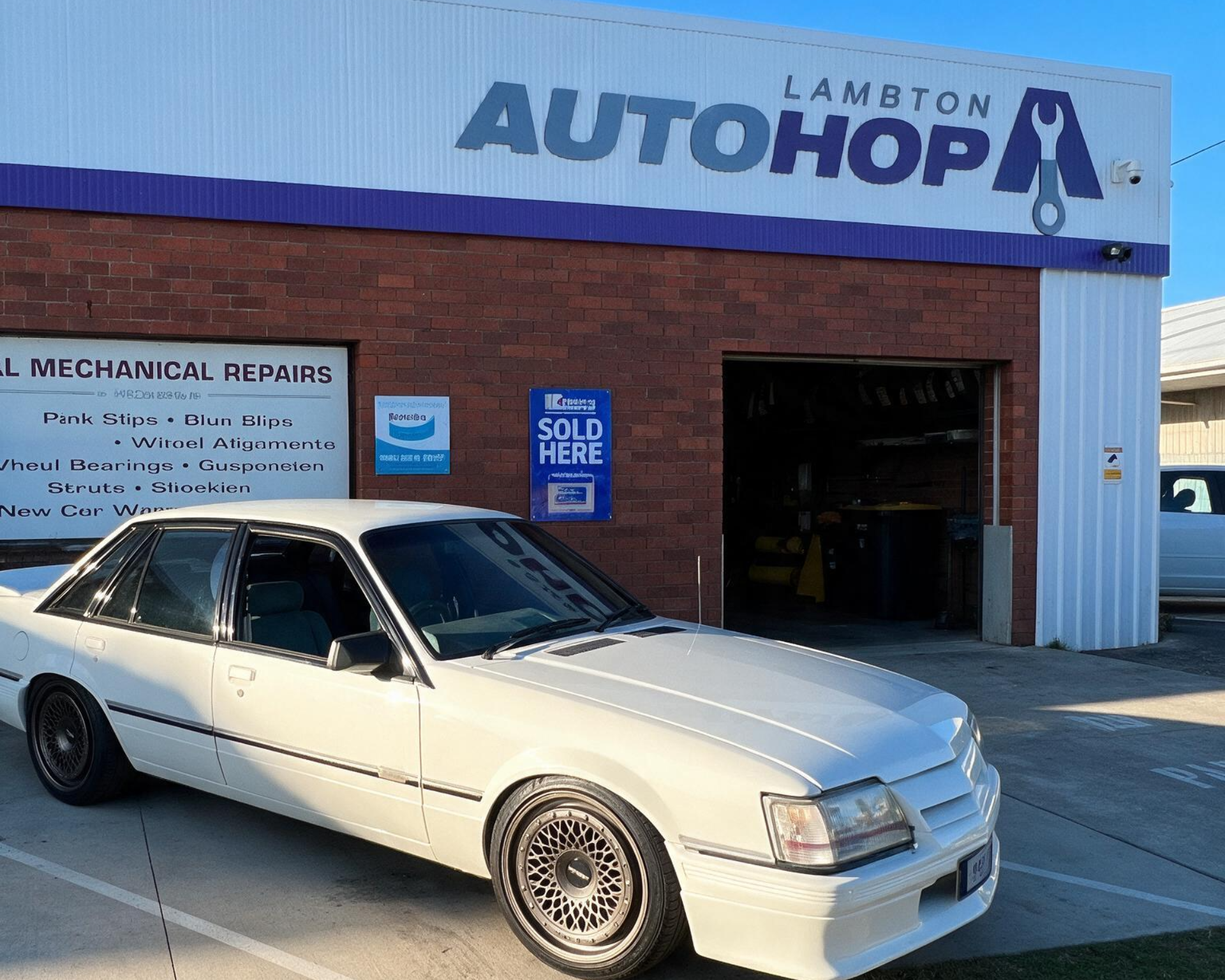 White sedan parked outside Lambton Autohop auto repair shop with open garage bay