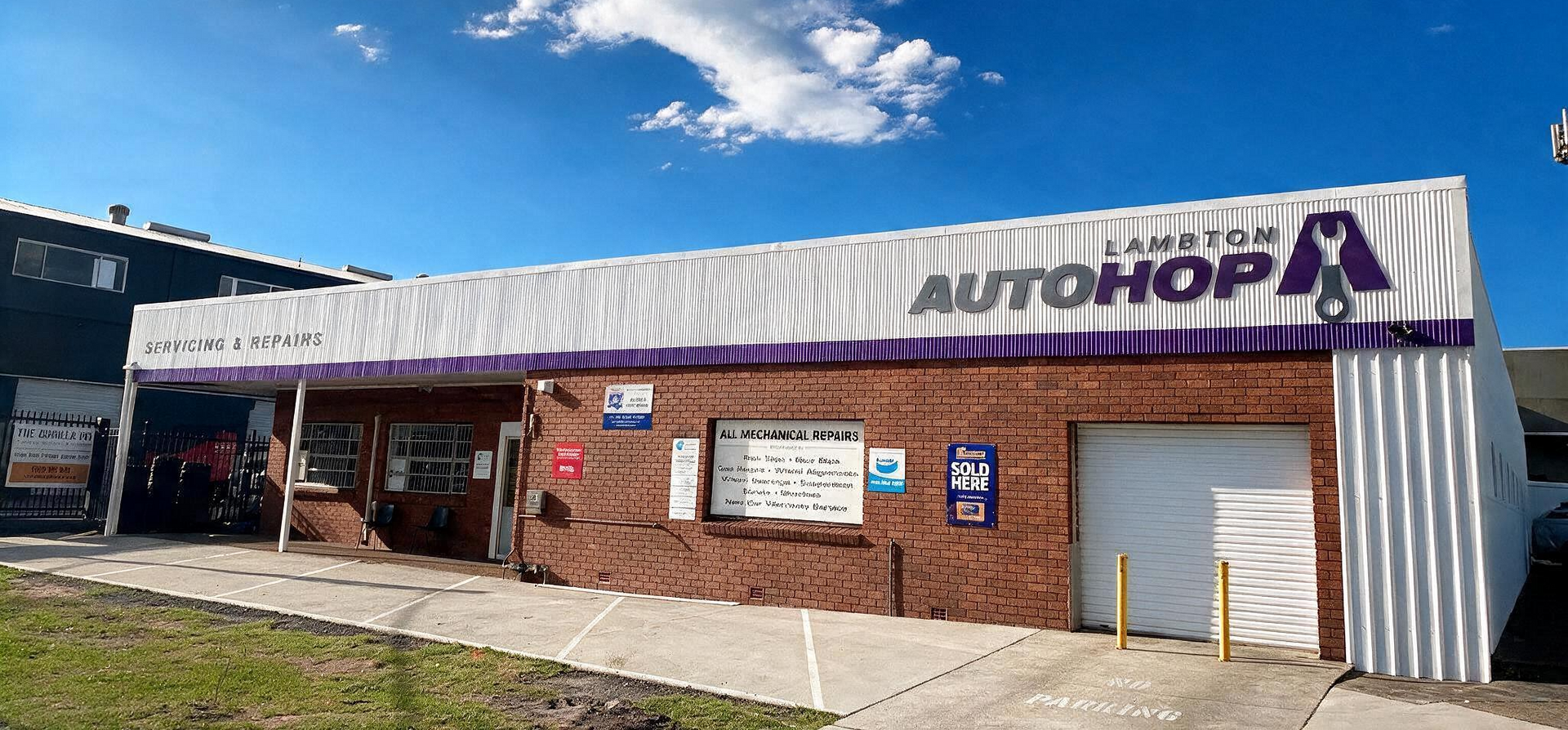 Two mechanics in purple shirts working under the hood of a car in a garage