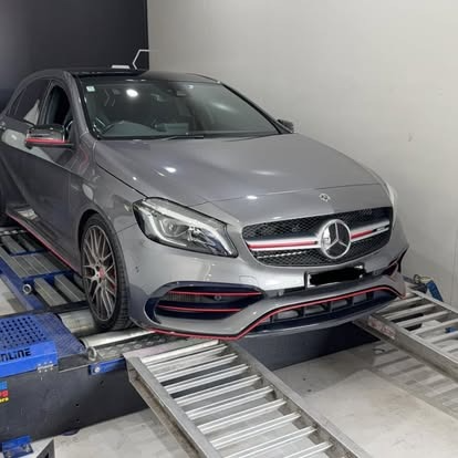 Silver Mercedes-Benz sedan on a dynamometer in a garage, with front wheels on metal rollers.