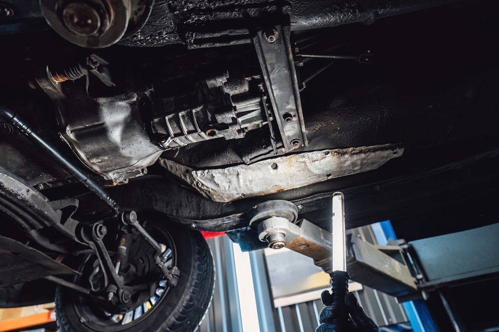 Undercarriage of a car on a lift in a repair shop, with tools visible nearby.