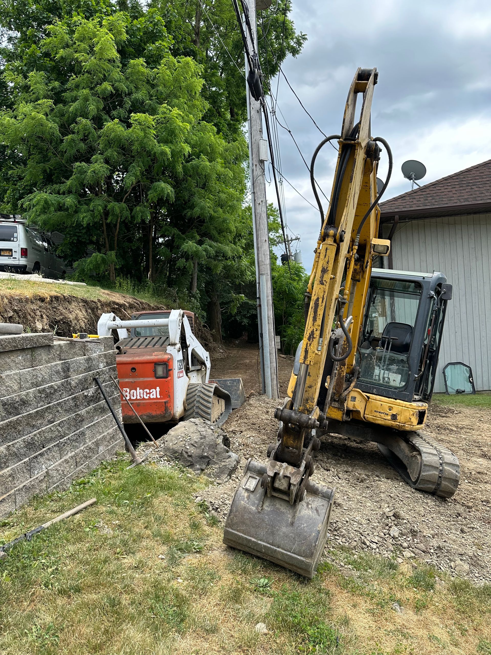 A yellow excavator is digging a hole in the ground in front of a house.