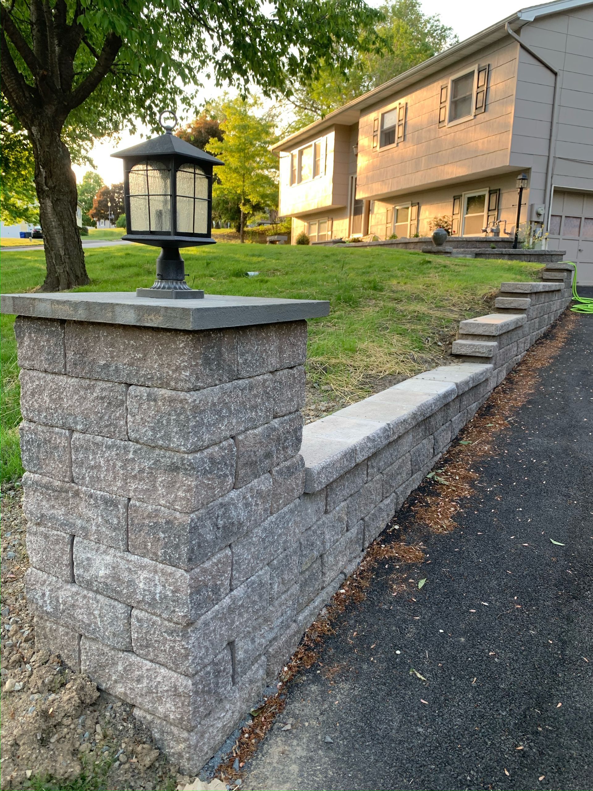 A brick wall with a lamp on top of it in front of a house.
