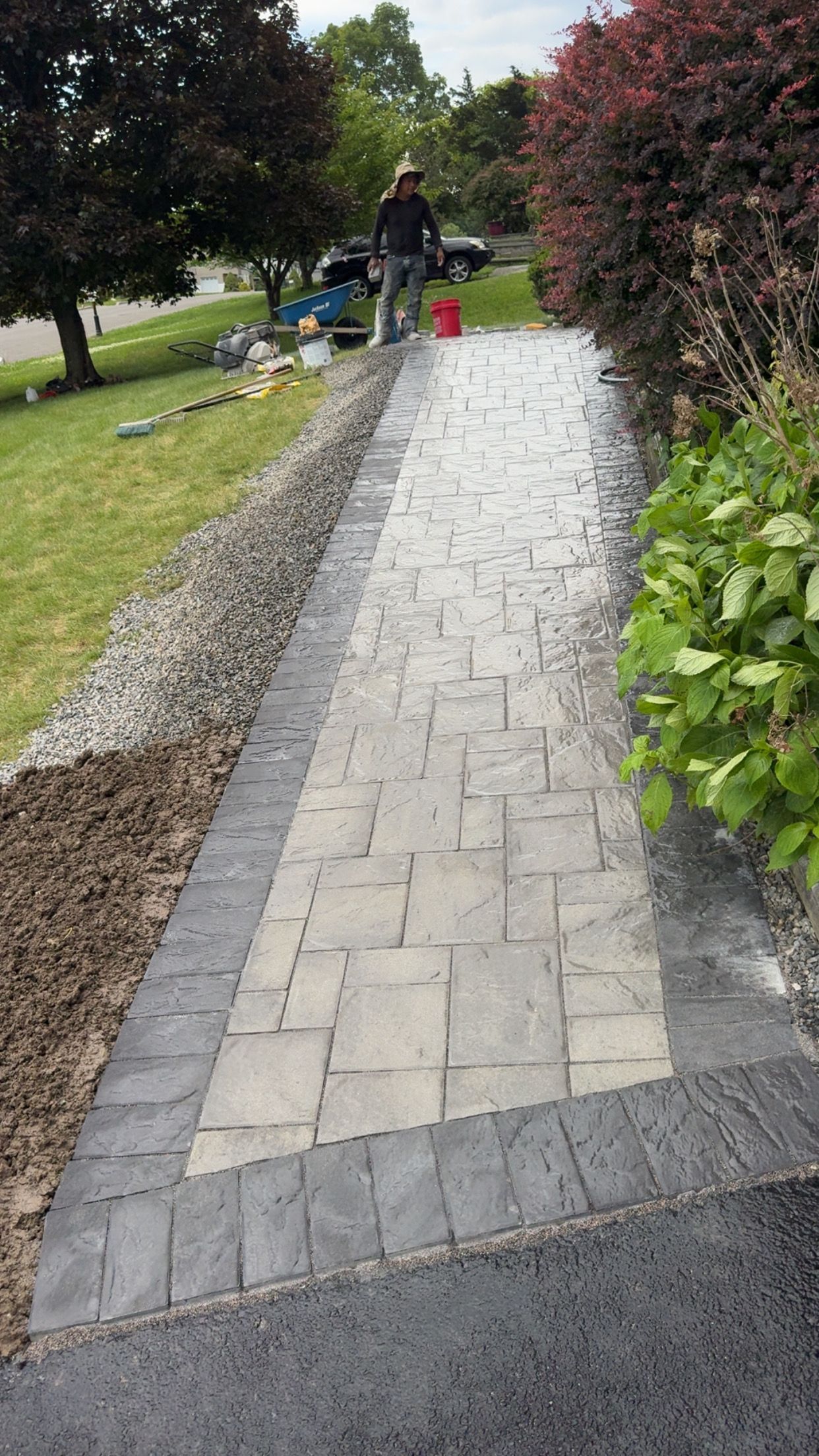 A man is standing on a sidewalk next to a driveway.