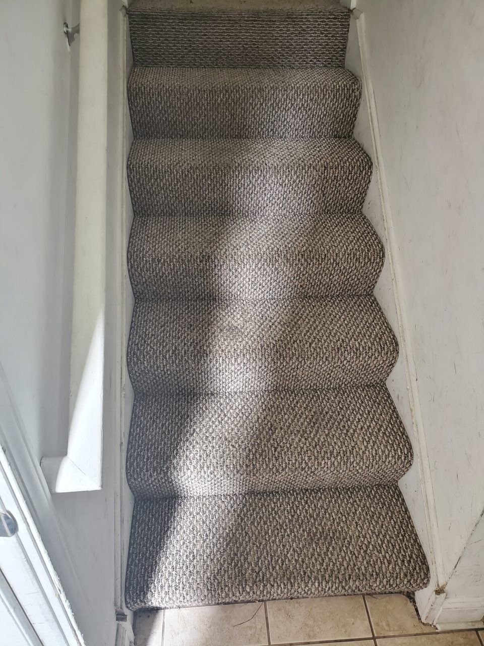 Carpeted staircase with light gray, textured steps; white walls.