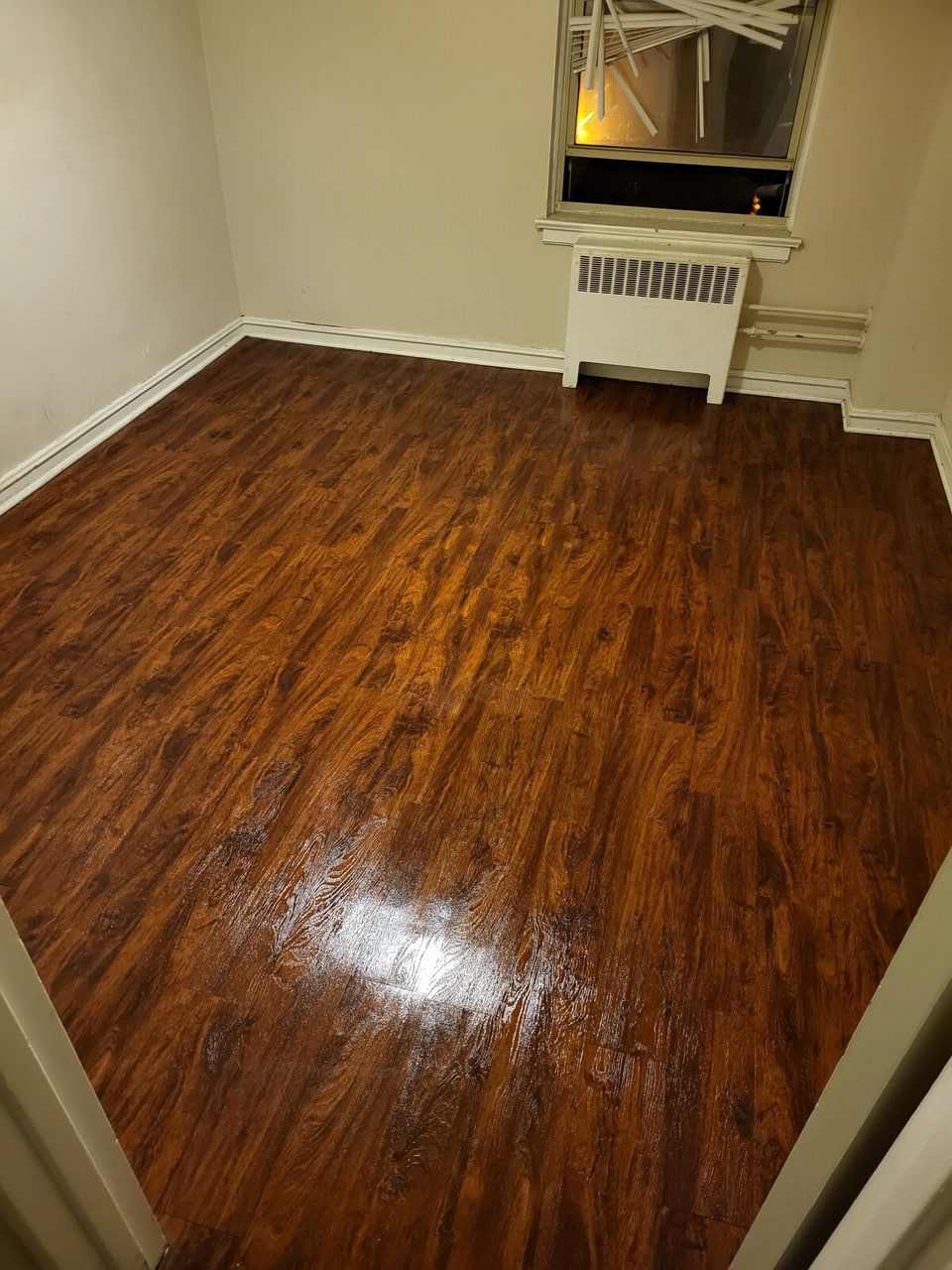 Room with glossy wood-like flooring, radiator under window, and beige walls.