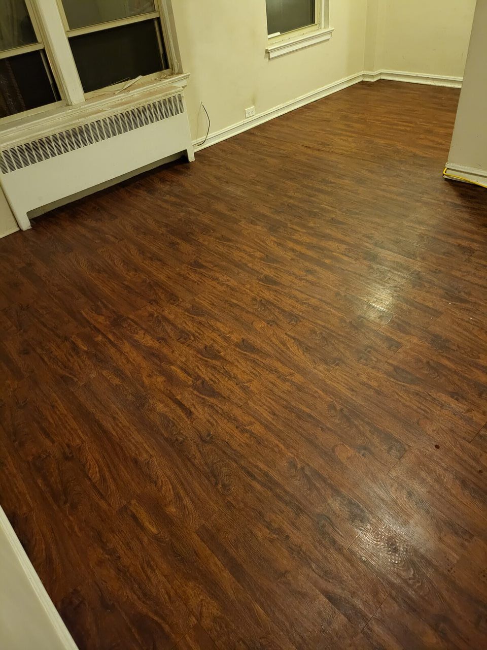 Dark brown wooden floor in a room with a window, radiator, and white trim.