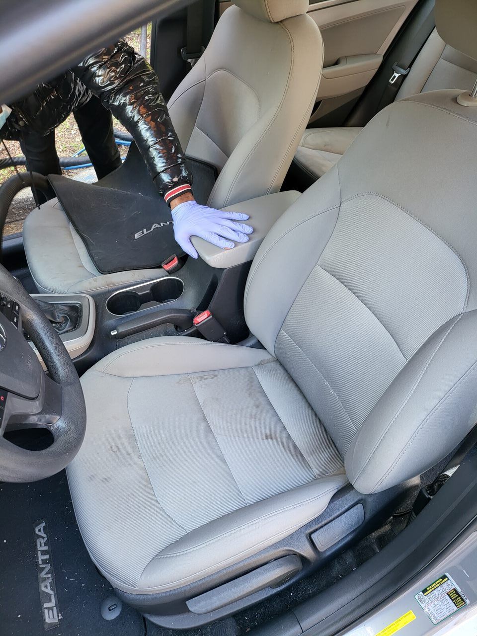 Person in a car wearing a sequined jacket and gloves, cleaning the light gray front seat.