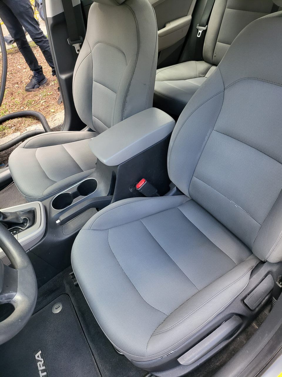Gray car interior with front seats, armrest, and cup holders.
