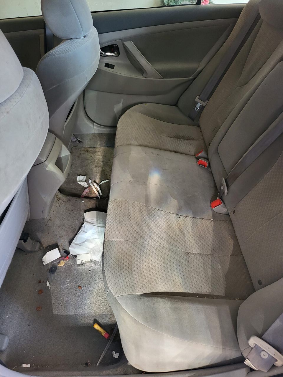 Dirty car interior, showing rear seats and floor with debris. Gray fabric seats, visible trash.