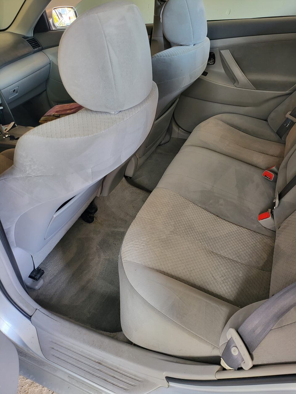 Back interior of a car with light gray seats and carpet. Two seat backs are folded down.