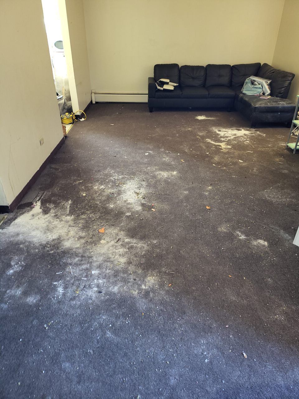 Dirty carpeted room with dark sectional sofa against a wall; debris scattered on the floor.