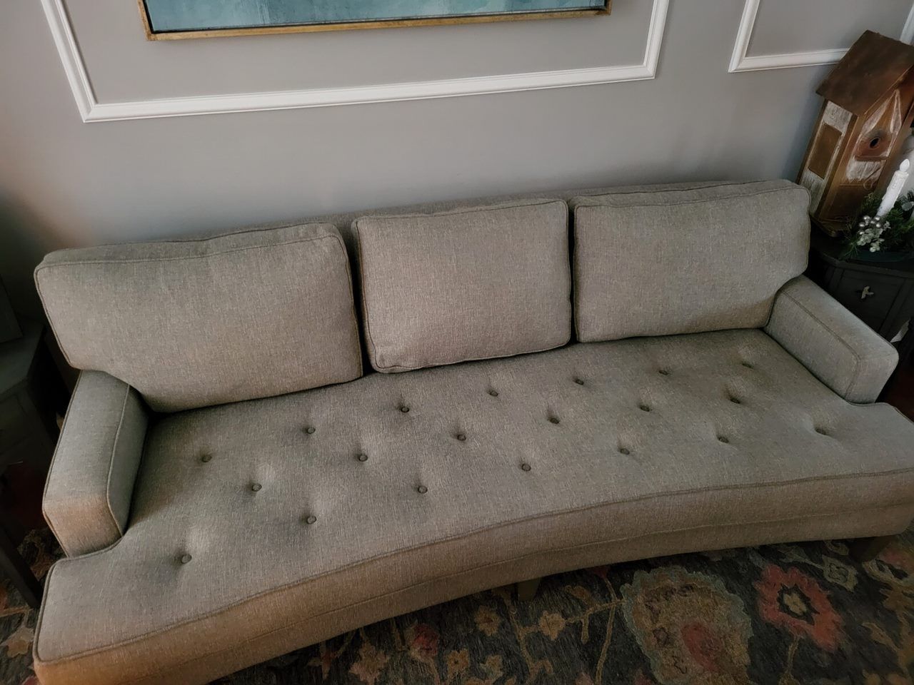 Gray, curved sofa with three back cushions and button detailing, set against a gray wall.