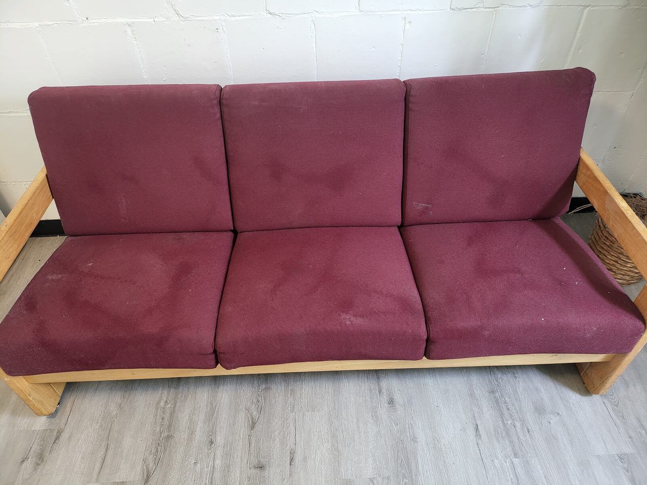 Three-seat sofa with reddish-purple cushions and light-colored wooden frame, set against a white wall.