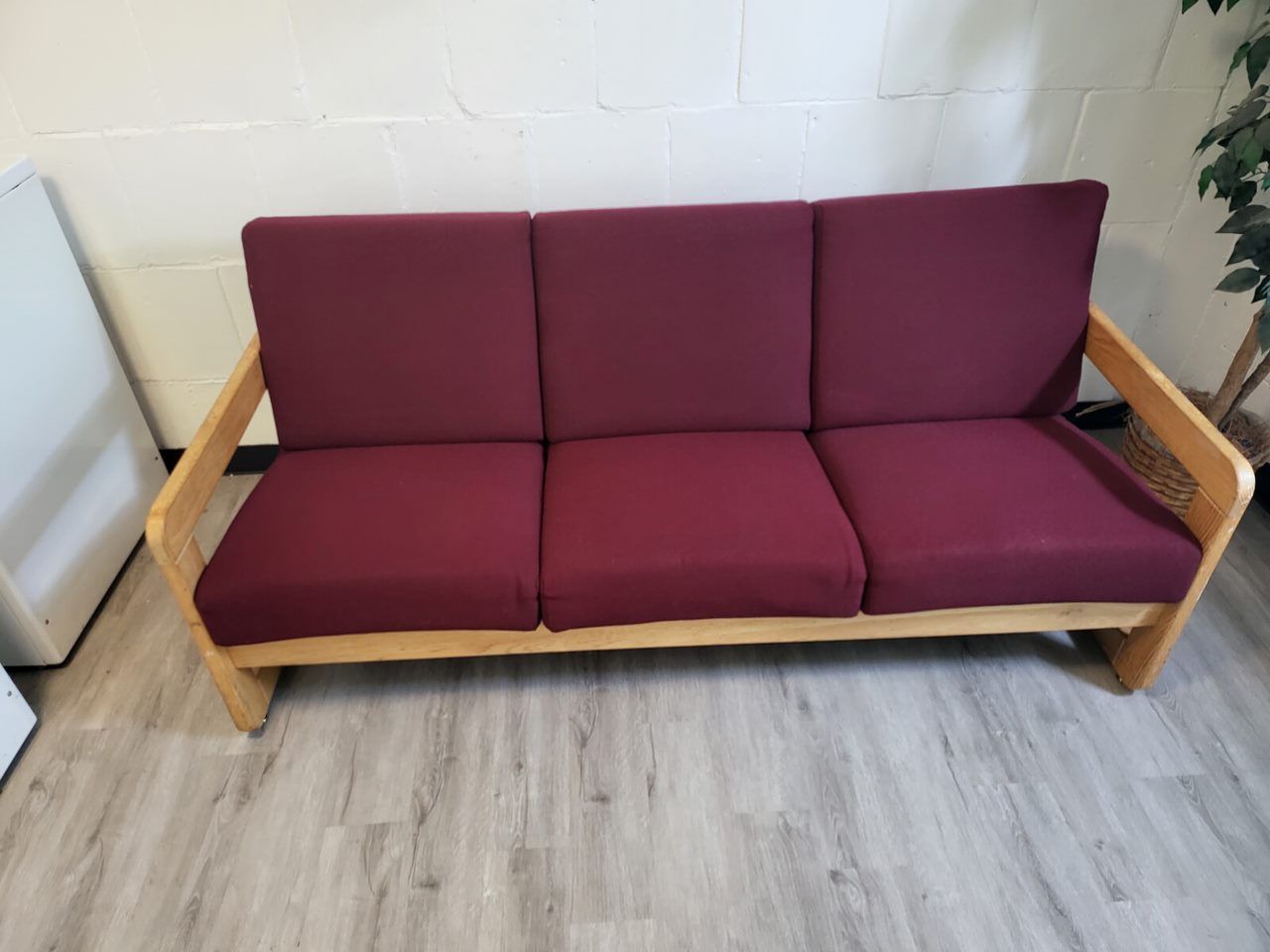 Three-cushion sofa with burgundy cushions and light wood frame against a wall and wood floor.