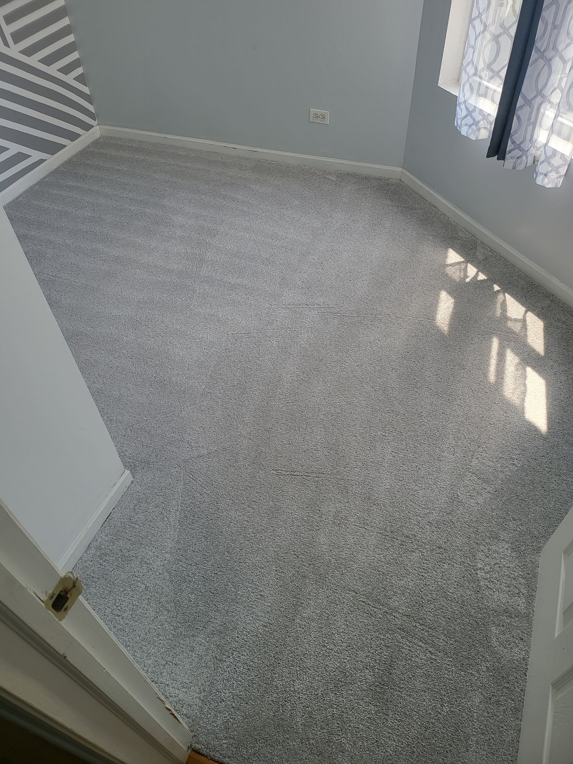 Grey speckled floor in a room with white walls, window, and patterned accent wall.