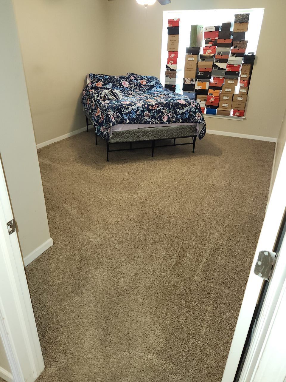 Bedroom with bed, bench, window with stacked shoe boxes, and tan carpet.