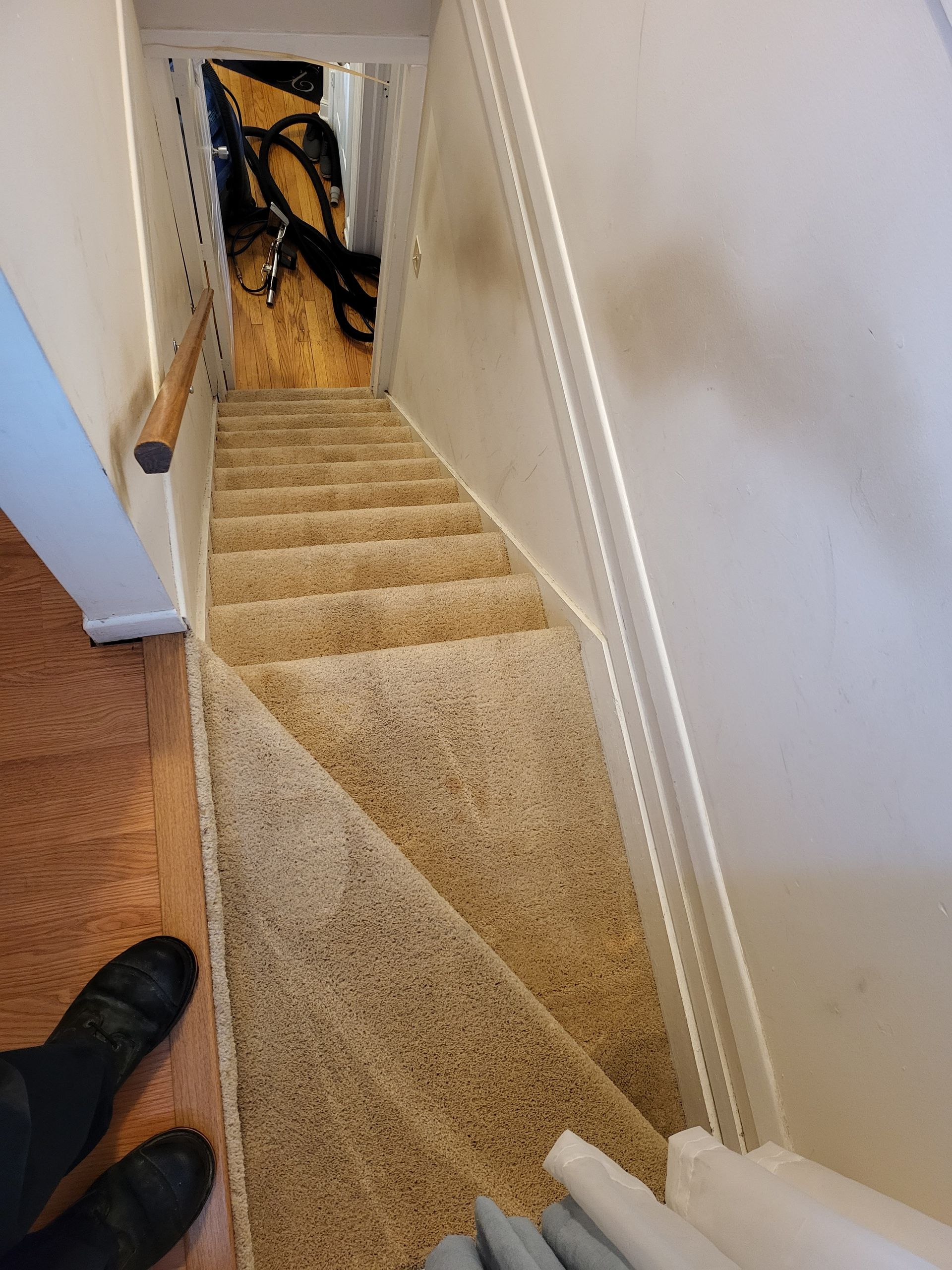 Staircase with beige carpet and white walls leading downward into a doorway with items stored inside.