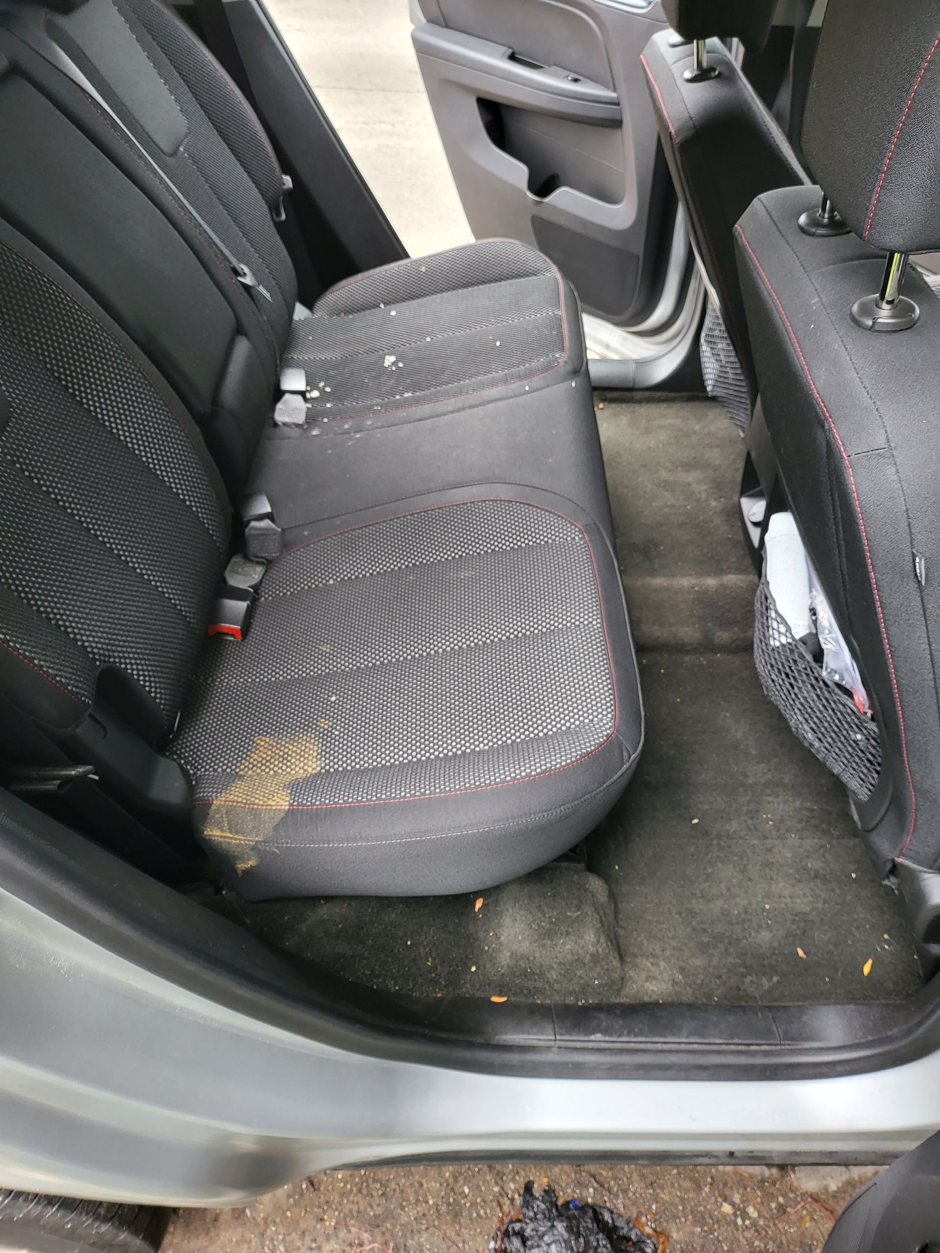 Dirty car interior with rear seats; grey upholstery, debris, and soiled carpet.