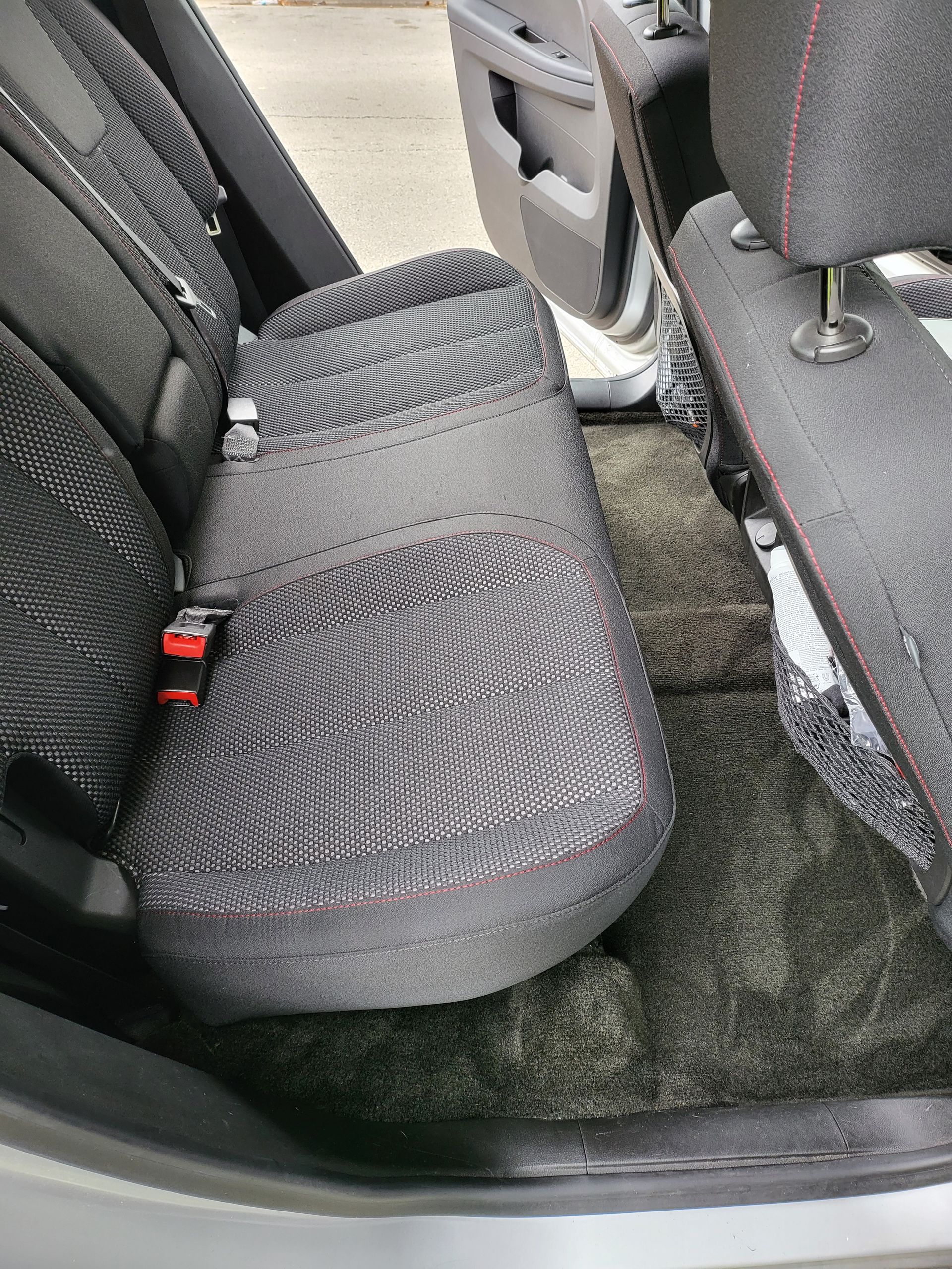 Car's back seat with detached seat cushion. Gray fabric seats, black carpet. Red stitching and seatbelt visible.