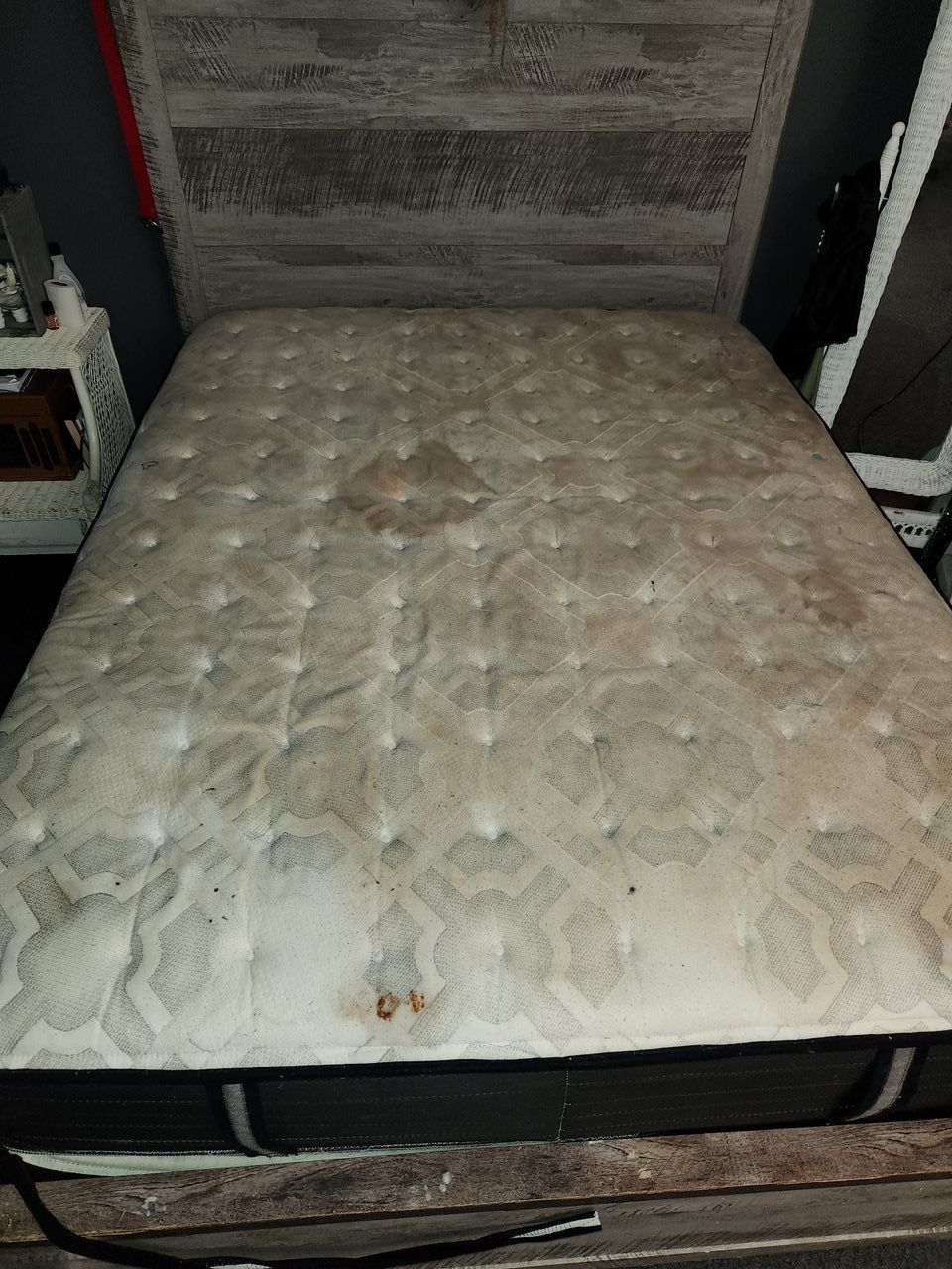 Dirty white mattress on a wooden bed frame, with stains and discolored areas.