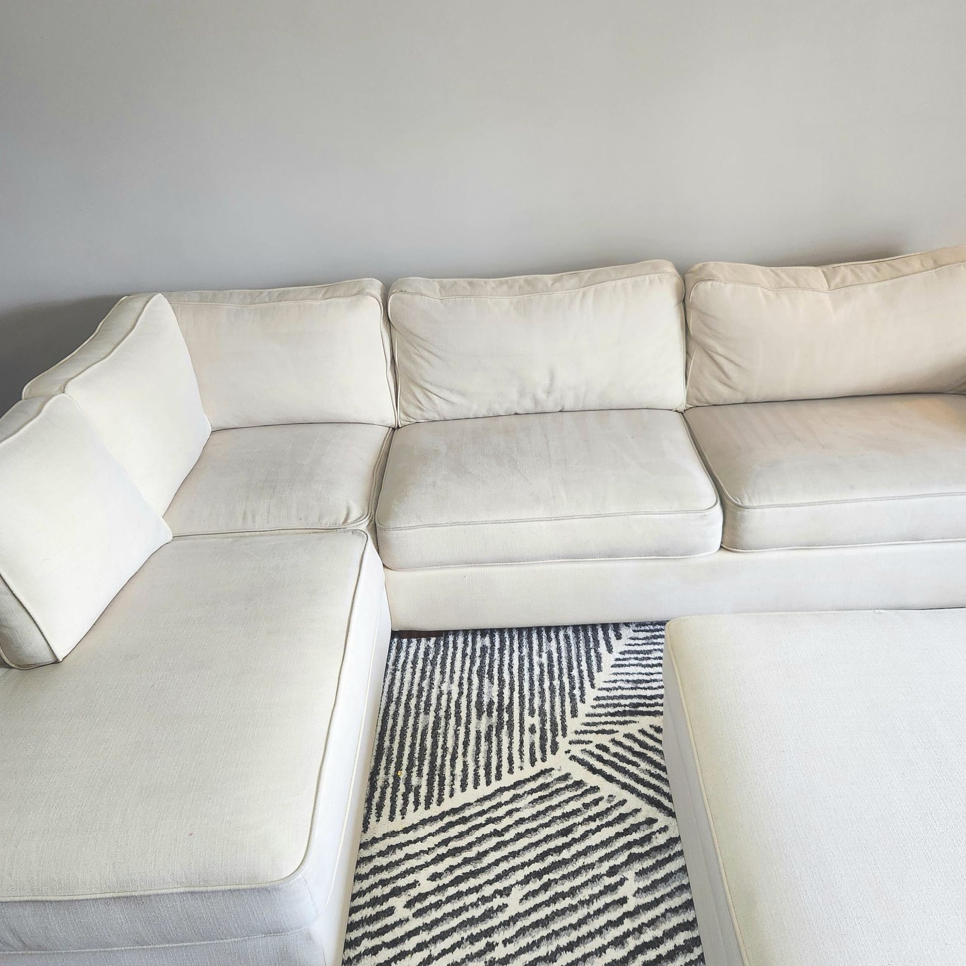 White sectional sofa on a geometric black and white rug against a gray wall.