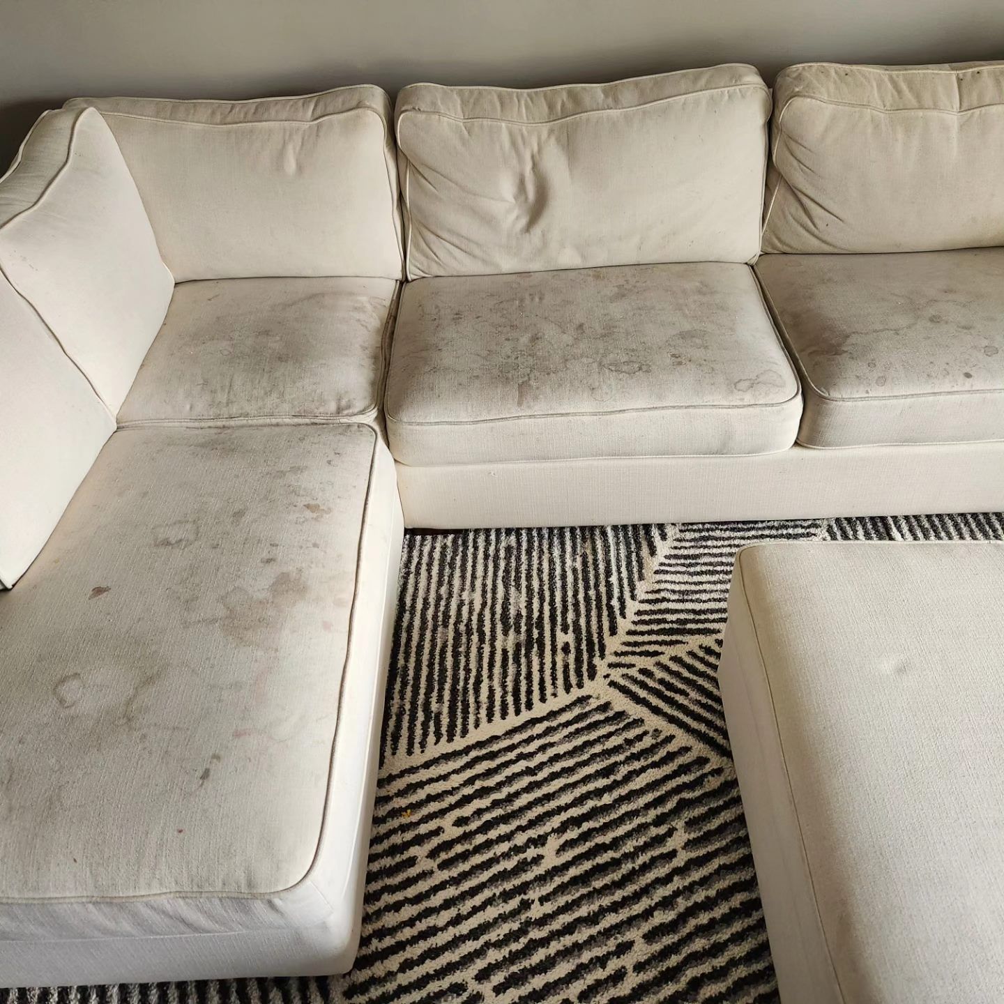 White sectional sofa with visible dirt and stains on cushions, next to a black and white rug.