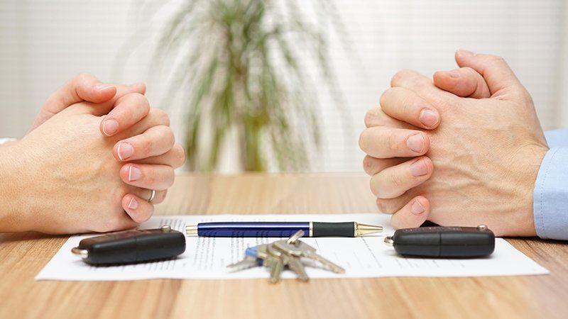 Two People's hands on a table with a paper, pen, and keys on the table