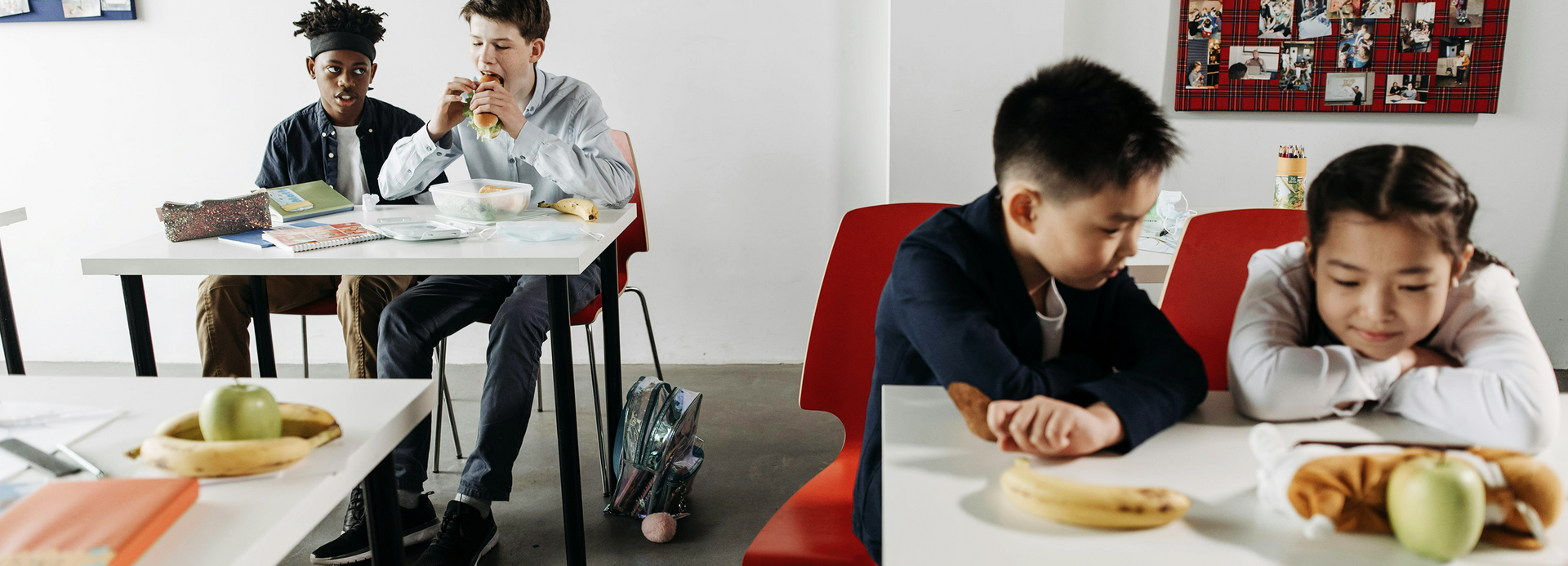 A group of children are sitting at tables in a cafeteria eating food.