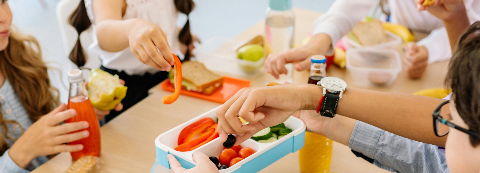 A group of children are sitting at a table eating lunch.