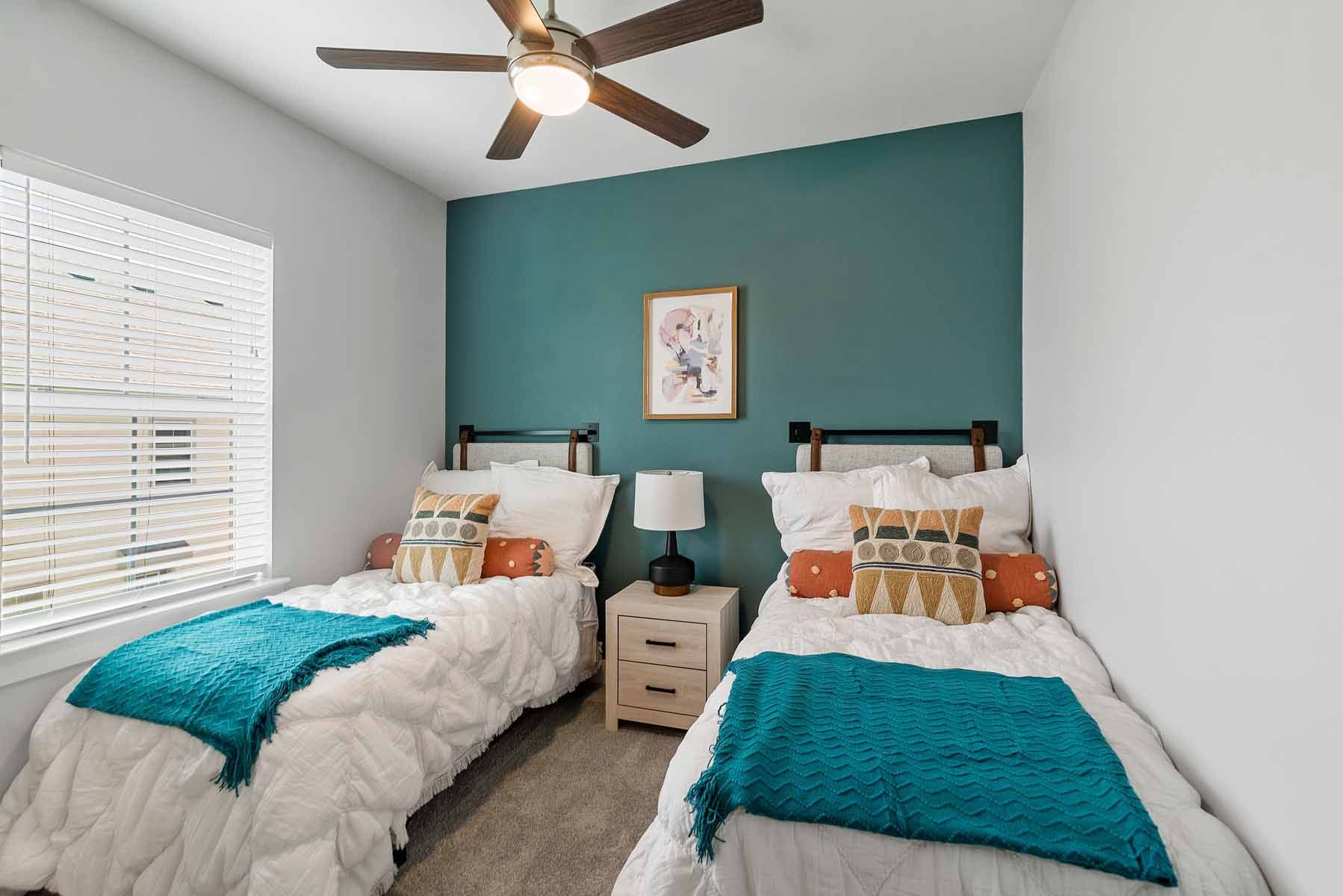 Two twin beds in a bedroom with teal accent wall, white bedding, and a ceiling fan.