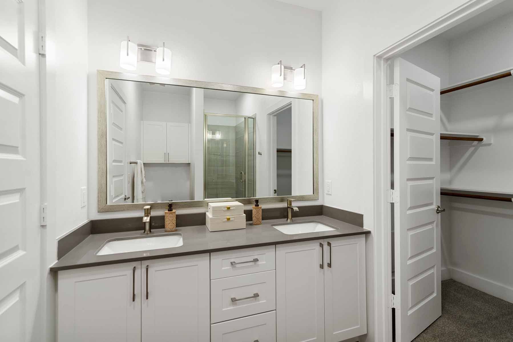 White bathroom with double vanity, large mirror, and walk-in closet.