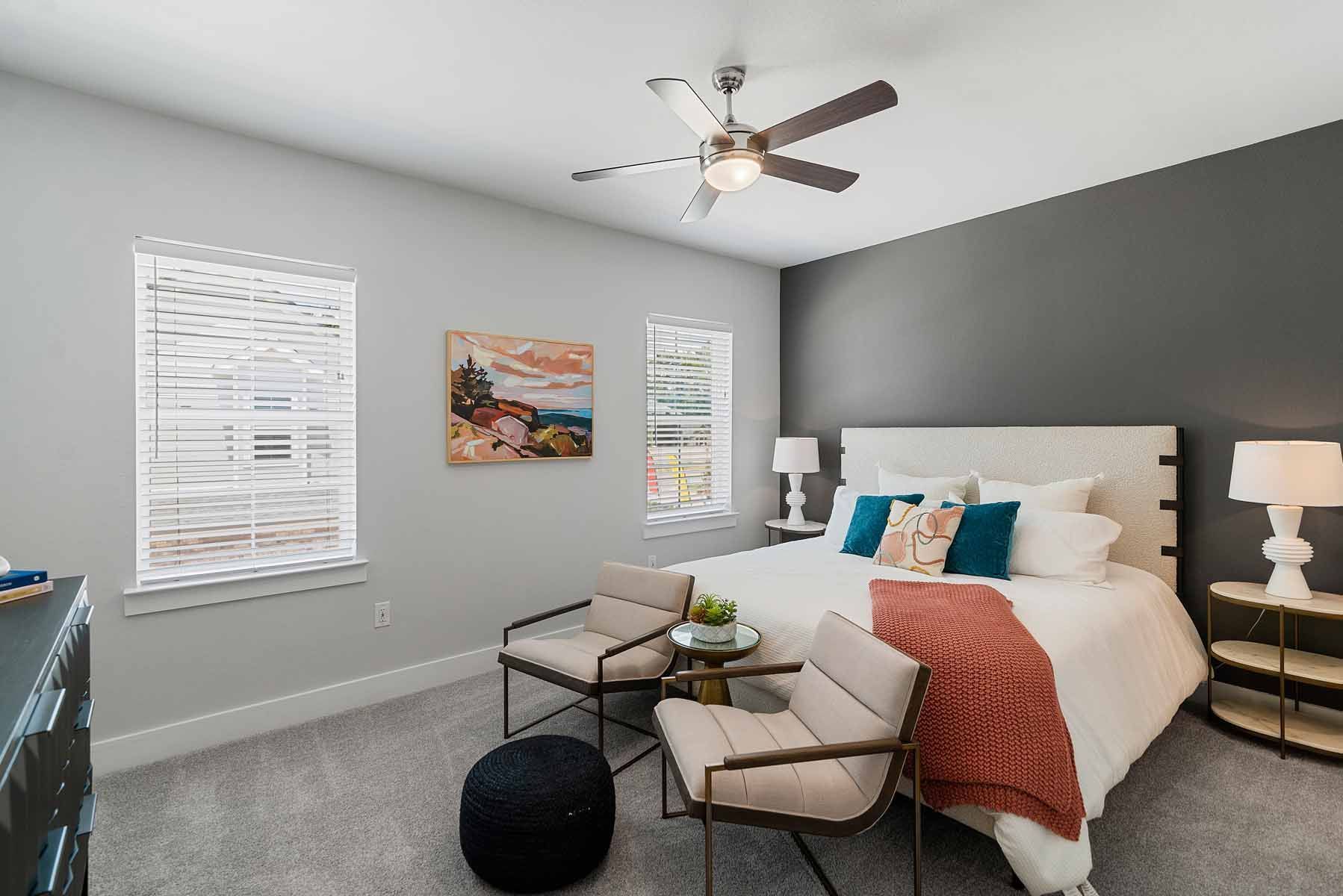 Bedroom with a gray wall, bed, two chairs, and a black ottoman.