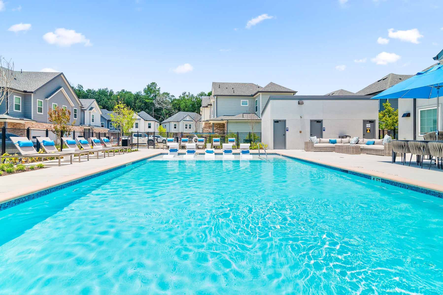 Spring, TX Luxury Apartments with In-Unit Washer and Dryer - Villas at Birnham Woods - A Swimming Pool Surrounded by Lounge Chairs and Modern Community Buildings.