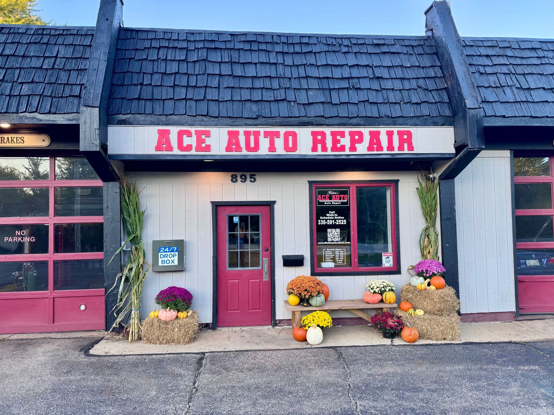 Small storefront with red door, bench, pumpkins, and window signage on a wet sidewalk. | Medina’s Ace Auto