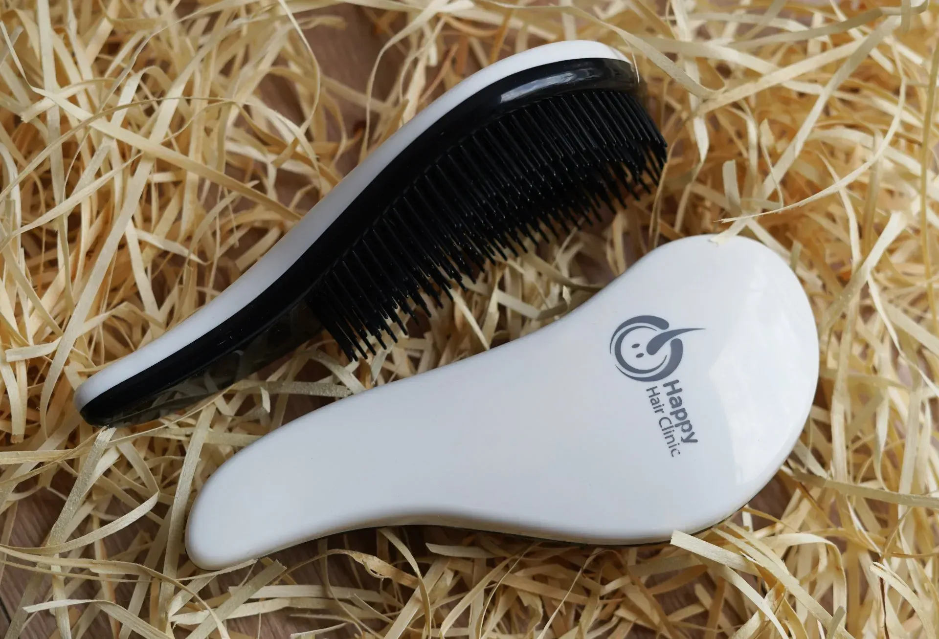 Peine y cepillo para cabello blanco y negro sobre un lecho de paja, con el cepillo con la marca